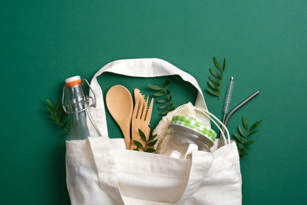 Reusable canvas shopper bag with eco friendly bamboo cutlery, metal drinking straws, glass jar and bottle. Zero waste, plastic free concept. Sustainable lifestyle