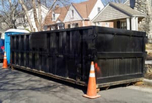 Black industrial dumpster container on neighborhood street.